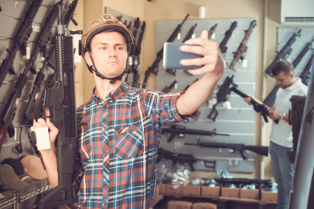 Young man taking selfie with pneumatic gun in military shop
