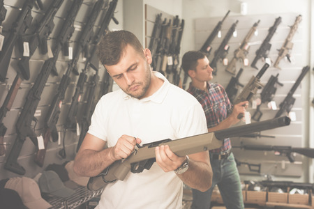 Two young men choosing air weapon in military shopの写真素材