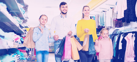 Young cheerful positive smiling parents with two little girls shopping in mall, carrying purchasesの写真素材