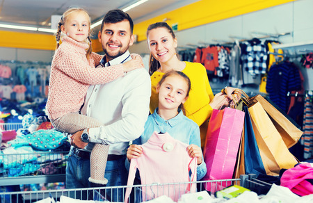 Young cheerful family with two daughters after shopping in clothes storeの写真素材