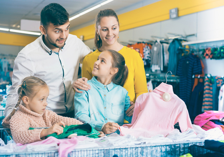 Happy adult family with two little girls choosing new clothes in mallの写真素材