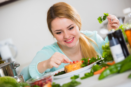 Pretty housewife decorating plate with vegetable salad and cheeseの写真素材