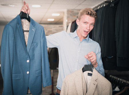 Consumer man holding on hanger colored jackets in the dress shopの写真素材