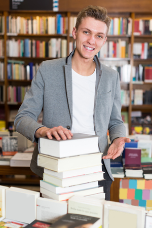 Portrait of young male with stack of textbooks in bookshopの写真素材