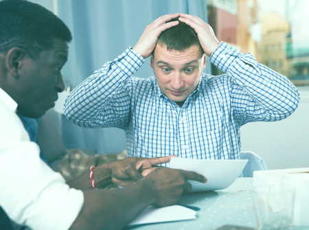 Upset two men in home interior, filling up documents indoorの写真素材