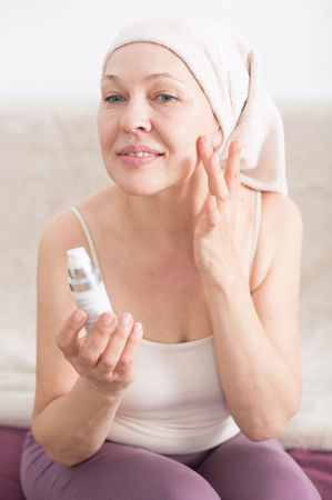 Elderly woman using face cream during beauty procedures at homeの写真素材