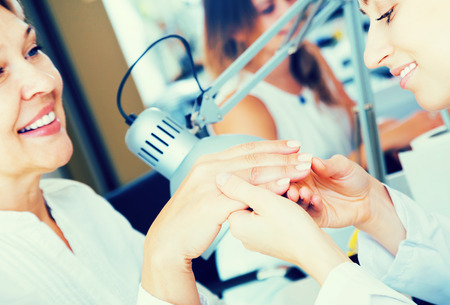 Aged woman client having manicure done in nail salon in close-upの写真素材
