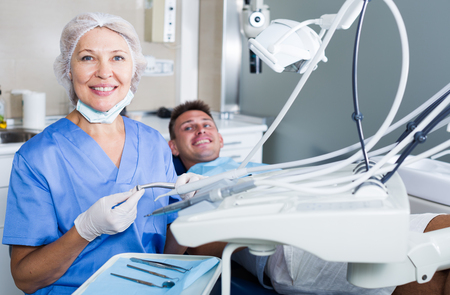 Confident female dentist in dental office with male patient in chairの写真素材