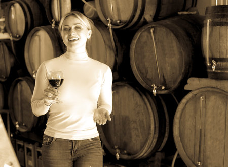 Portrait woman having  glass of wine and standing next to woods in wine house