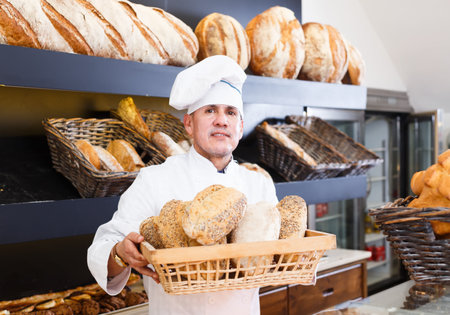 smiling bakery male worker with tasty and fresh bread products on counter in the shop