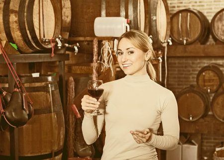 Attractive woman having glass of wine and standing next to woods in wine house 