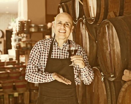Positive male wine maker taking wine from wood in wineryの写真素材