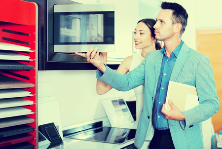 Young glad cheerful positive couple choosing microwave in household appliance section in furnishing storeの写真素材