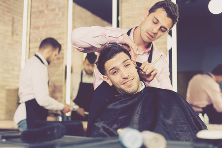 Handsome young man during beard shaving by professional barber in barbershopの写真素材