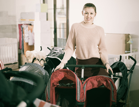 Happy  positive  female choosing carriage for twins in the children's storeの写真素材