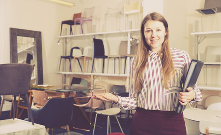 Young attractive salesgirl with folder in hands inviting to visit furniture salonの写真素材