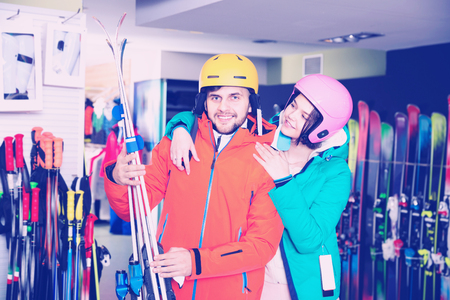 Smiling  positive young man and woman standing with purchased ski equipment in shopの写真素材
