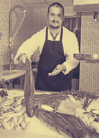 Laughing seller in black apron showing fish in handsの写真素材
