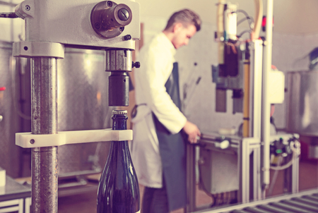 Glad cheerful male worker corking wine bottles with machine at sparkling wine factoryの写真素材