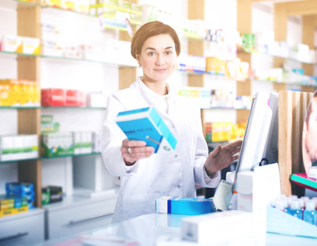 Young woman pharmacist ready to assist in choosing at counter in pharmacyの写真素材