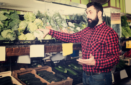 Smiling man seller showing cauliflowers in grocery shopの写真素材