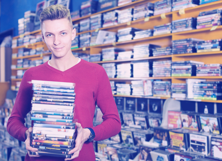 Portrait of smiling young male holding stack of DVDs in shop indoorsの写真素材