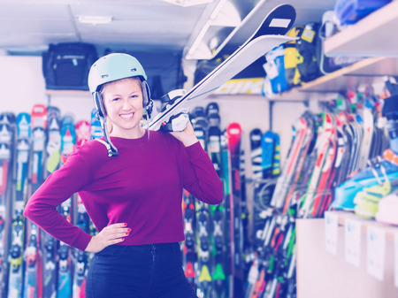Portrait of young customer female in ski helmet who is showing ski in storeの写真素材