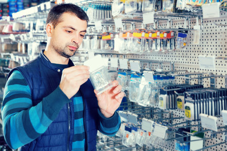 calm male customer choosing fishing hooks near stand in the sports shop indoorsの写真素材