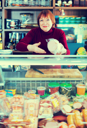 Glad female selling sausage and ham at the counter in supermarketの写真素材