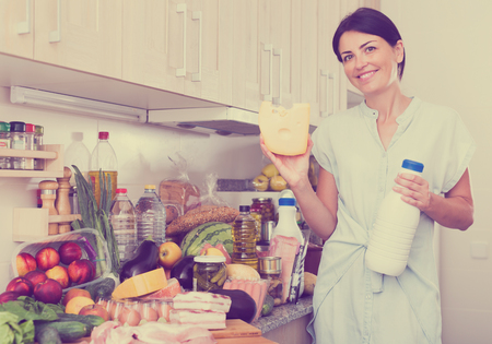 Woman is posing with milk and cheese in time cooking on the kitchen at home.

の写真素材