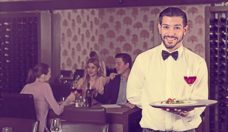 Glad bearded waiter with serving tray welcoming to restaurantの写真素材