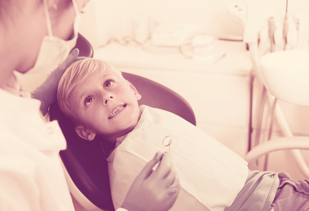 Dentist in white is taking a view of an adult teenager on the chair in hospital.の写真素材