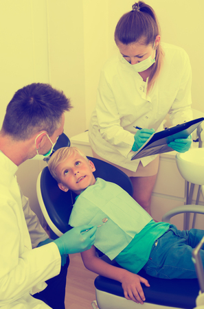 Male dentist with assistant are diagnosticating to young patient which is sitting in dental clinic.の写真素材