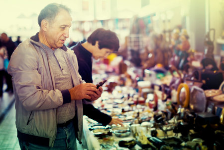 Ordinary man and woman choosing interesting souvenirs at traditional flea market