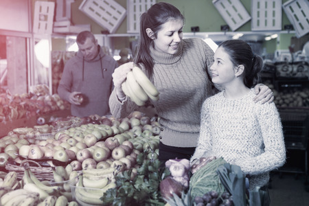 Smiling girl and young female looking for fresh delicious fruits during family shoppingの写真素材