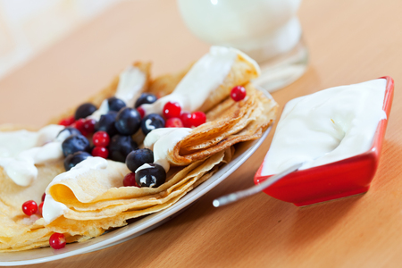 Closeup of  delicious breakfast.  Sweet pancakes with berries on white plate and dairy cream at table ready for eatの写真素材