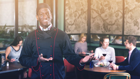 Smiling happy politely African American chef inviting to visit cozy restaurant