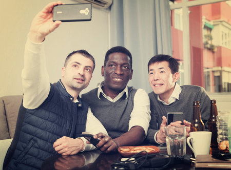 Three cheerful male friends making selfie during bachelor gathering at home