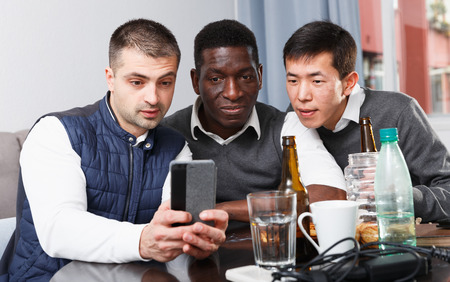 Three men are looking in mobile and resting together at home.の写真素材