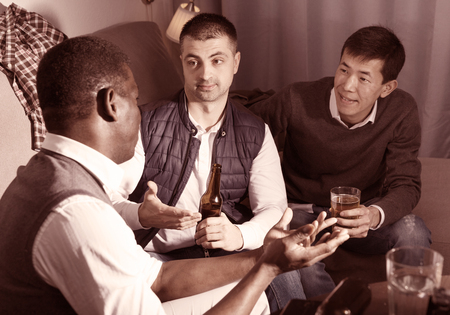 Three men are drinking beer and talking about life in time rest together at home.の写真素材
