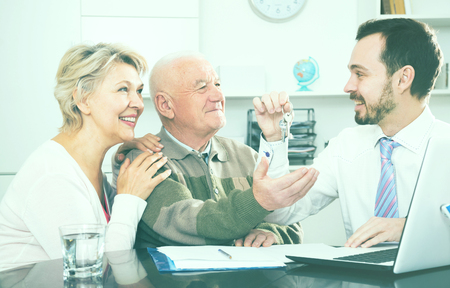 Mature woman and elderly man signing purchase and sale agreement of apartment and hand over keysの写真素材