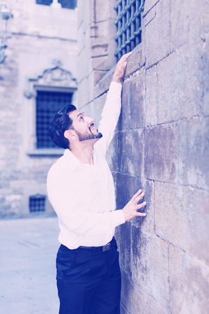 Handsome bearded man trying to climb stone wall to his belovedの写真素材