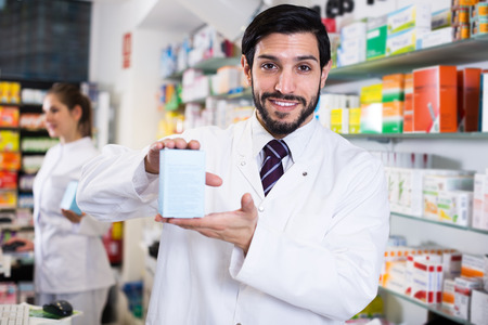 Smiling man pharmacist is standing with medicines in drugstoreの写真素材