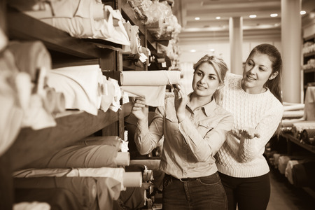 Two cheerful young female friends looking for interesting cloth in textile shopの写真素材