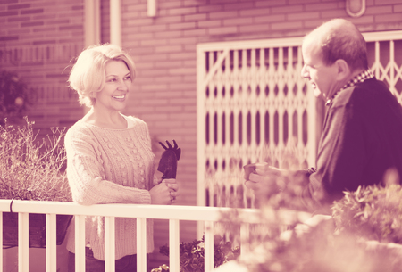 Mature smiling woman talking with male neighbor at balconの写真素材