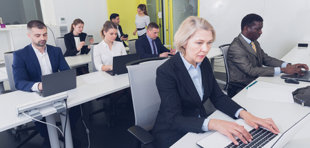 Senior businesswoman concentrated on work with laptop in coworking space with international teamの写真素材