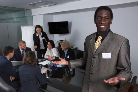 Portrait of smiling African American businessman with working team behind in conference roomの写真素材