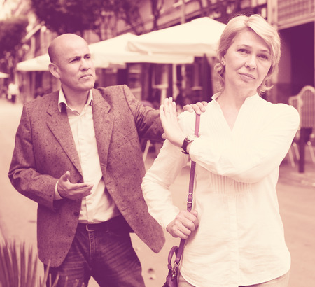 irritated senior woman standing back to man trying to talk outdoorsの写真素材