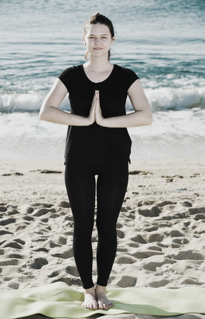 Girl in black T-shirt is staying and doing meditation on the beach near sea.の写真素材