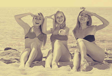 three cheerful  smiling girls in bikini relaxing on sandy beach on sunny day の写真素材